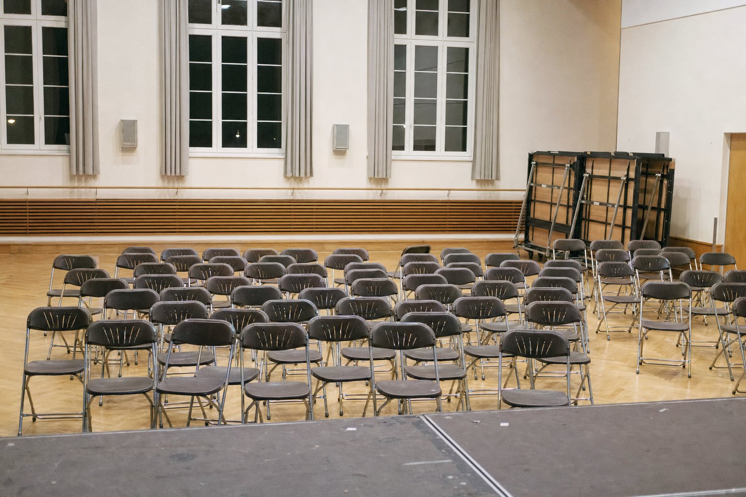 Salle communale après un événement, lumière de salle allumée, rangées de chaises pliantes vides