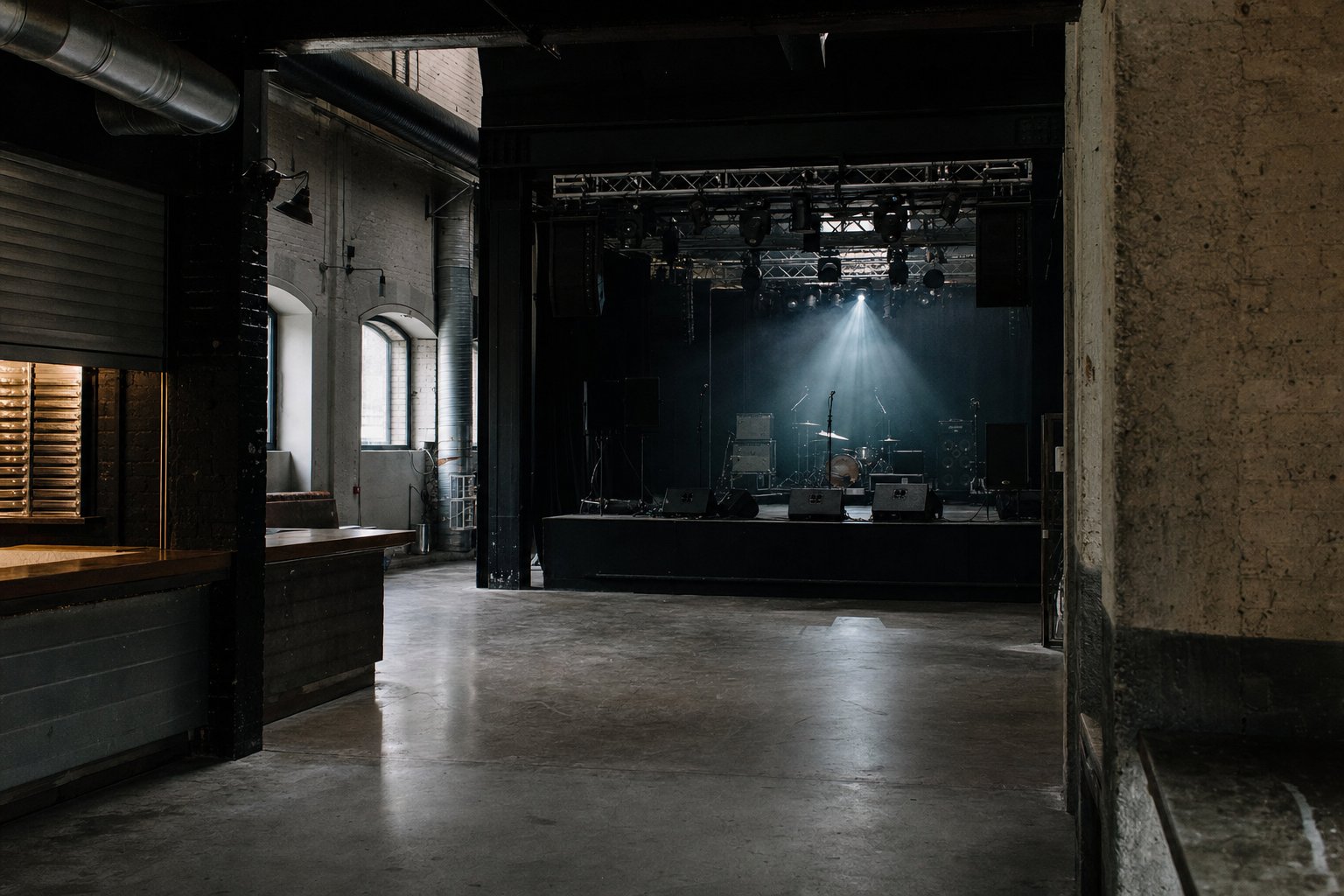 Salle de concert indépendante vide dans un bâtiment industriel reconverti, scène basse et sol debout