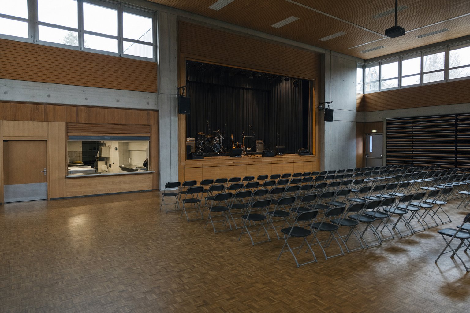 Intérieur d’une salle communale polyvalente préparée pour un concert, chaises pliantes et gradin replié