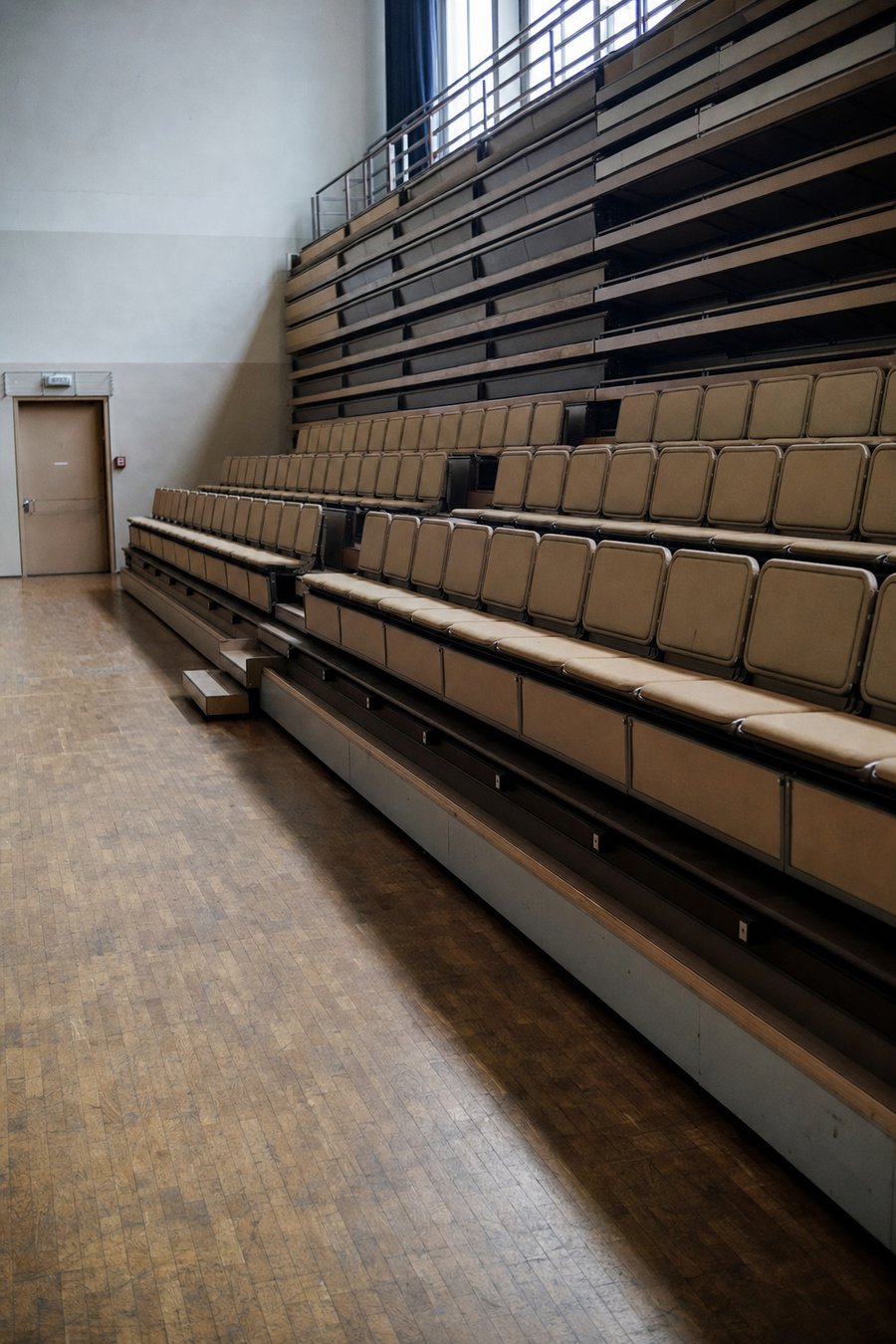 Gradin rétractable à demi déployé dans une salle communale, devant le parquet nu de la zone debout